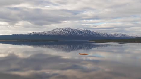 parallax drone shot of swedish lake with snowcapped mountains and cloudy sky