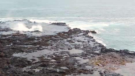 HD-Slow-motion-Hawaii-Kauai-static-overlooking-ocean-swirling-up-through-hole-in-lava-rock-in-left-of-frame-and-Spouting-Horn-blowhole-going-off-in-right-of-frame,-take-one