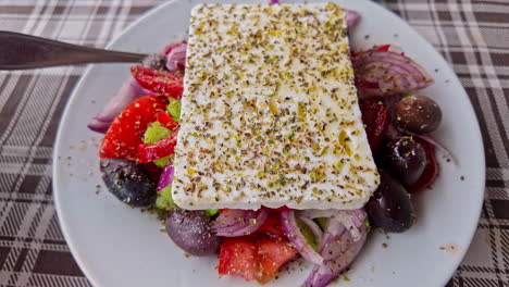 Close-up-of-Greek-salad-with-feta-cheese-topped-with-herbs-on-a-plaid-tablecloth