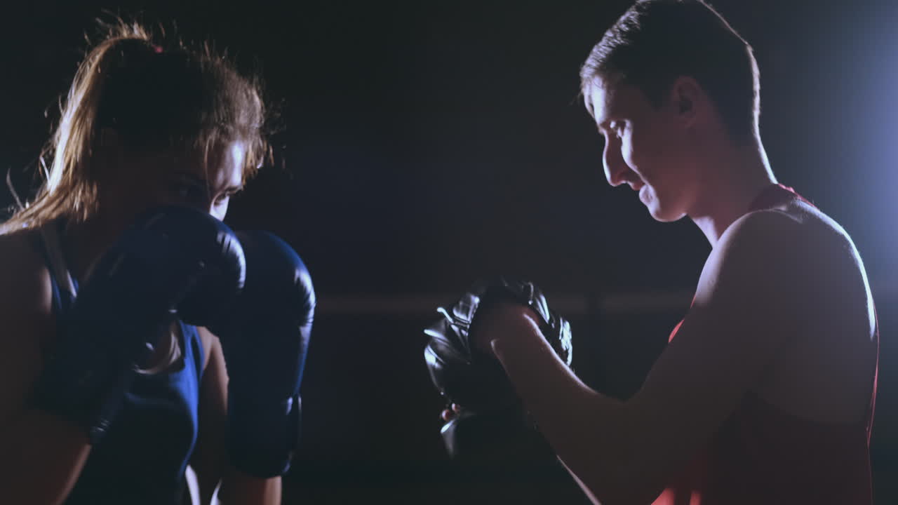 boxeadora golpeando unos guantes de enfoque con guantes de boxeo en un gimnasio ahumado