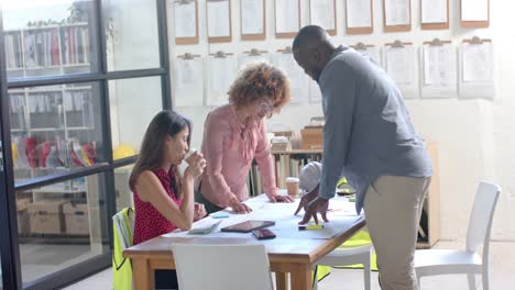 Busy-diverse-architects-discussing-blueprints-on-table-in-office,-slow-motion