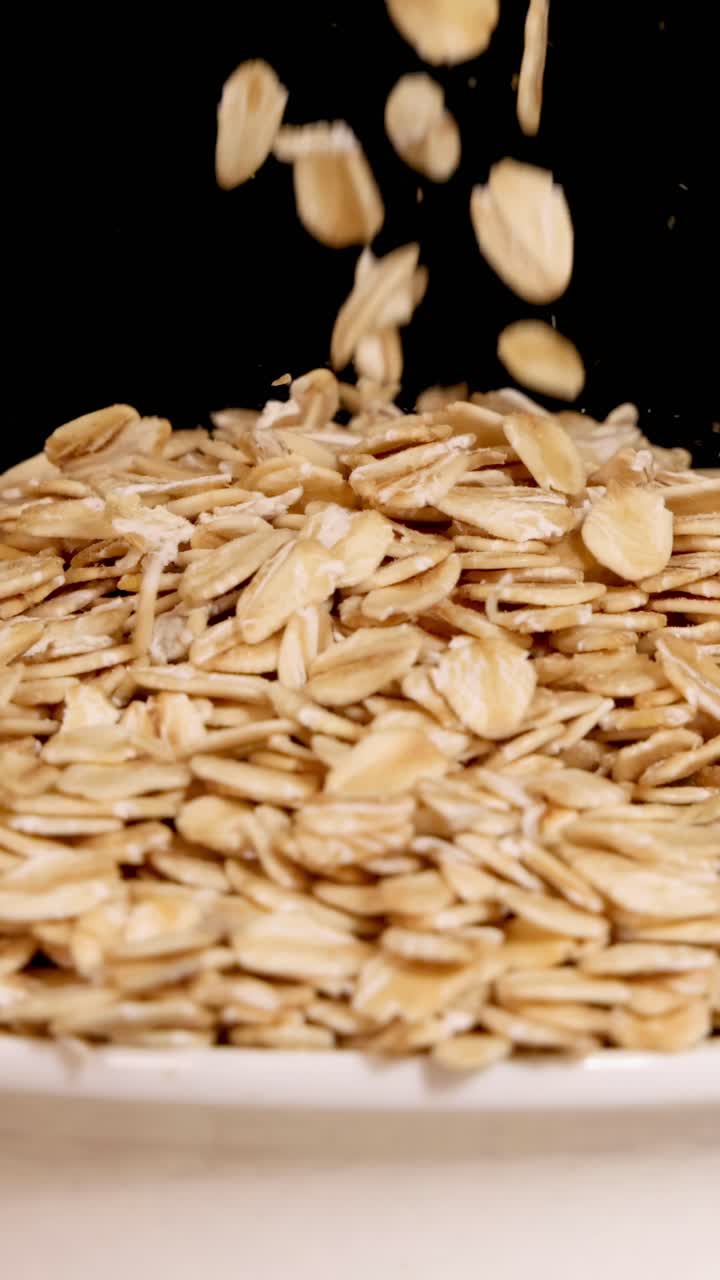 Chicchi d'avena cadono a cascata in una ciotola su uno sfondo nero, ripresi al rallentatore con illuminazione drammatica