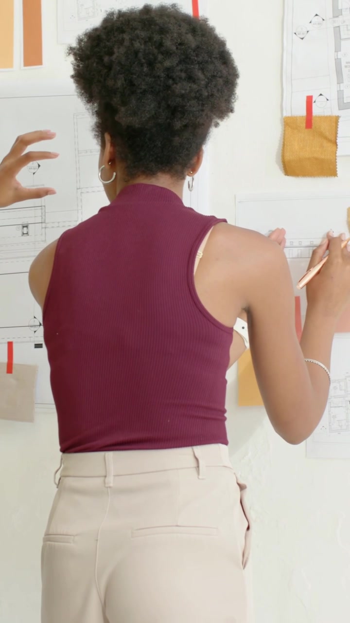 Vídeo vertical: Designer de cor bordô gravando amostras de cores, anotando o layout no estúdio enquanto colega entrega uma xícara