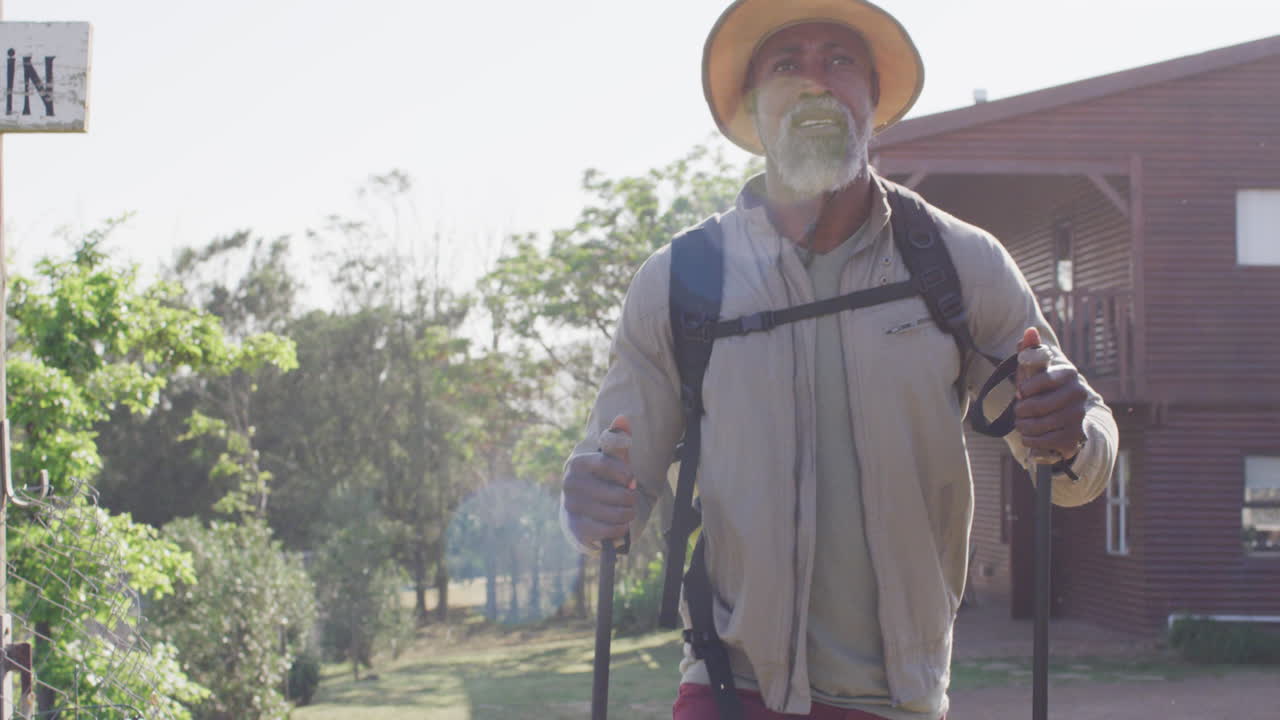Senior african american man hiking with trekking poles on sunny day, slow motion