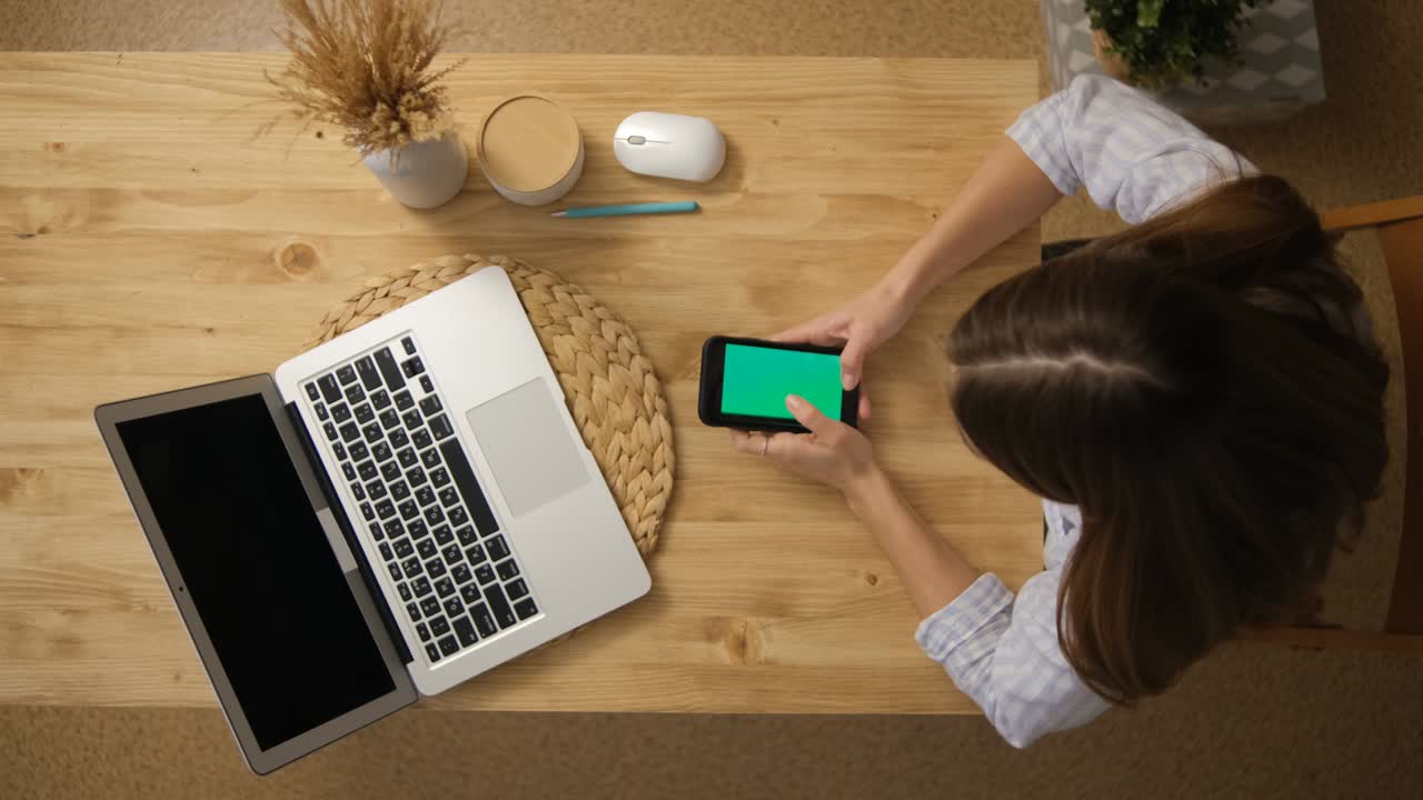 The girl is surfing on the Internet. Social network. The green screen of the phone monitor. A laptop. Top view. Remote training.