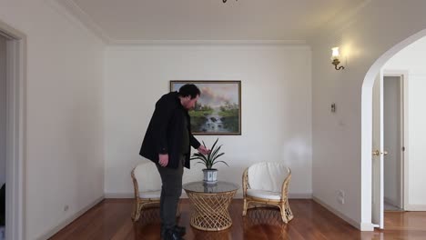 hombre entrando en una pequeña sala de estar y tocando una planta de hoja verde en una maceta