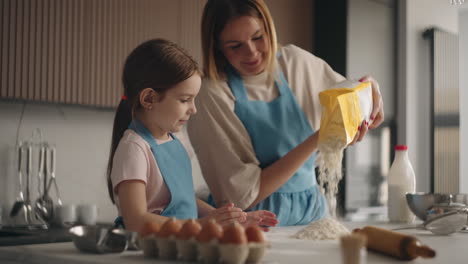 mother and child are cooking in home woman is pouring flour on table little girl helping to cook