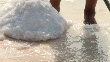 barefoot feet of a man next to heap of salt being removed from the salt pan, traditional work in the process of making natural salt