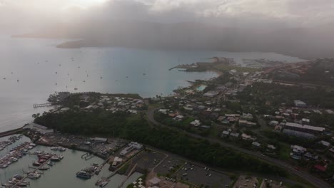 Port-Airlie-Beach-Bay-Lagoon-Coral-Sea-marina-aerial-drone-raining-cloudy-sunrise-morning-heart-of-Great-Barrier-Reef-Whitsundays-Whitehaven-jetty-yachts-sailboats-buildings-forward-motion