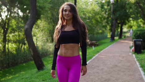 beautiful brunette woman in short sport top walking in the park after intensive training. fit healthy sport woman exercising in