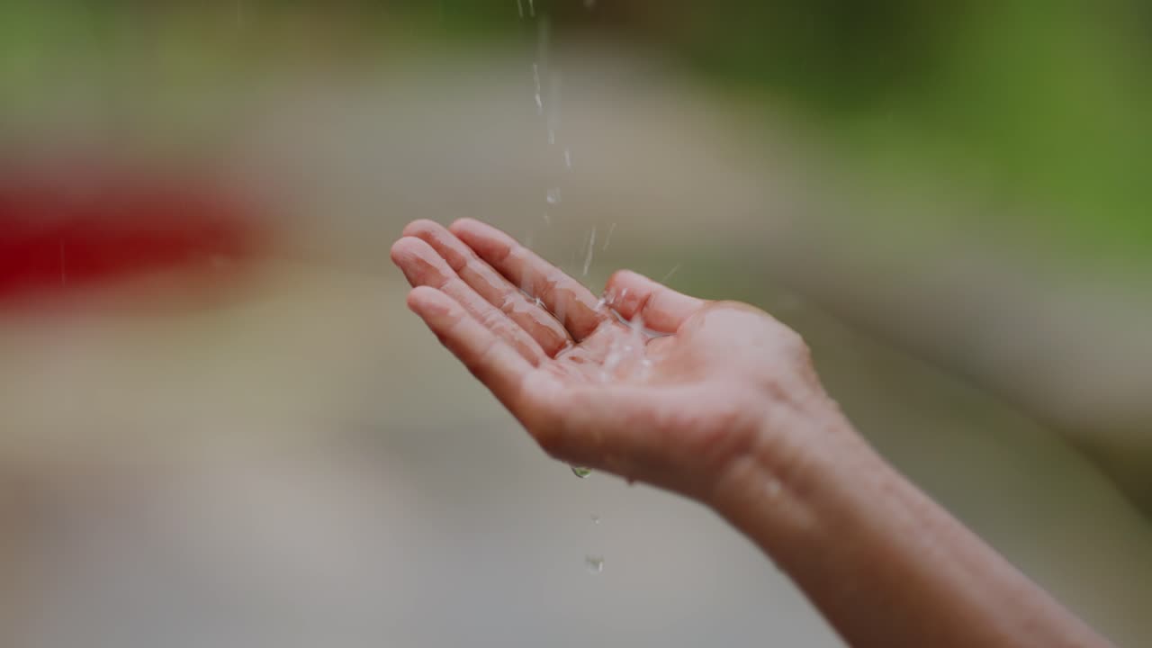Slow motion shot of open hands catching rainwater, symbolizing freedom and joy during village monsoon, 4k video