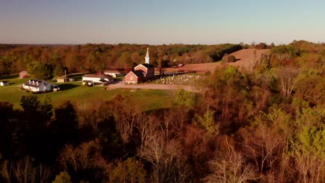 Areal-shot-of-forest,-cemetery,-and-farm-in-small-country-community-on-a-beautiful-fall-morning-at-sunrise