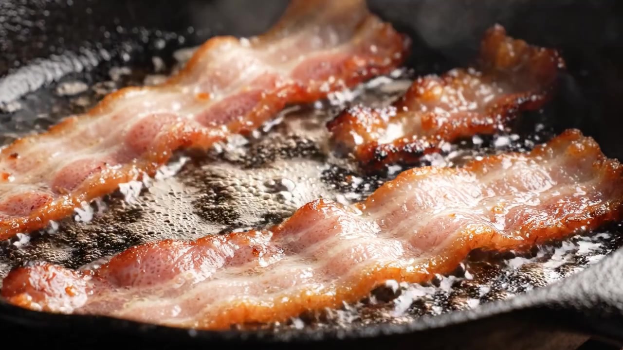 Pancetta Deliziosamente Sfrigolante in una Padella di Ghisa Catturata in Due Fotogrammi, che Mostra la Consistenza Croccante Perfettamente Cotta e la Lucentezza Irresistibile delle Striscioline di Pancetta.