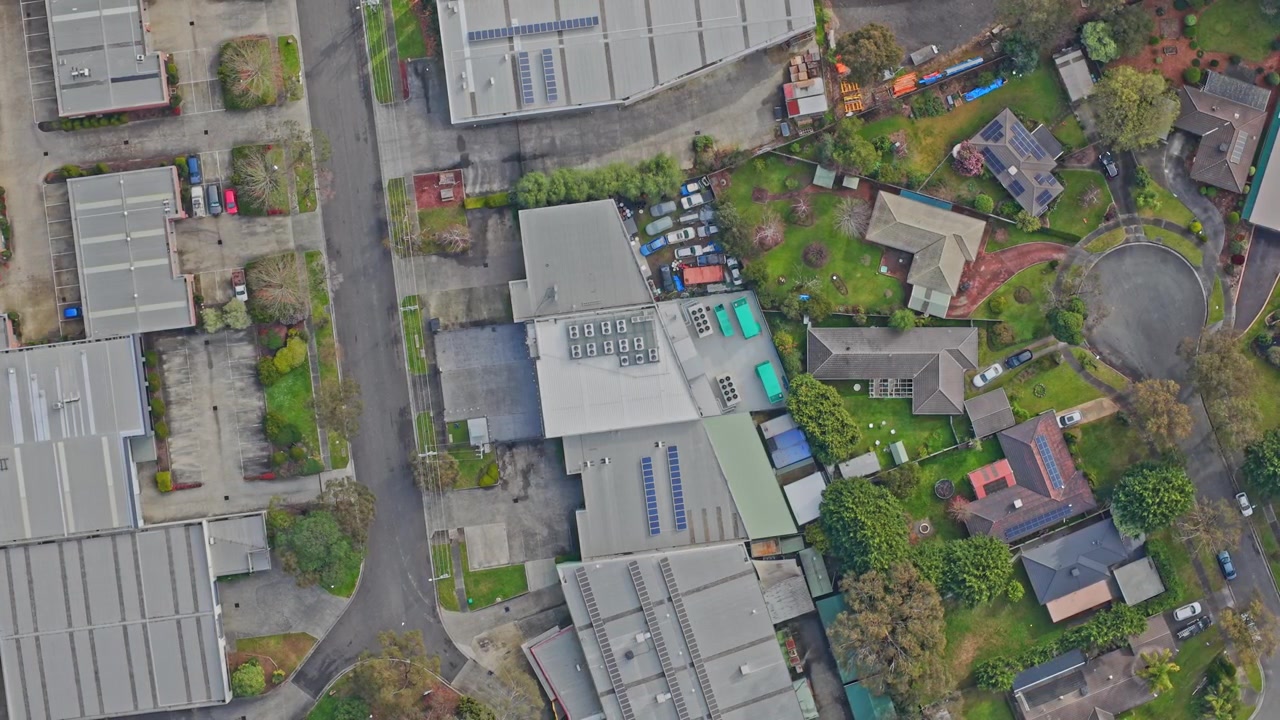 Højopløselig dronevideo viser et moderne datacenter med solpaneler på taget, omgivet af grønne landskaber og nærliggende kontorer i blødt dagslys. Statisk indramning ovenfra.