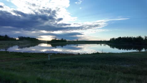 a peaceful sunset over a still lake in a rural russian setting, with beautiful reflections of the clouds in the water