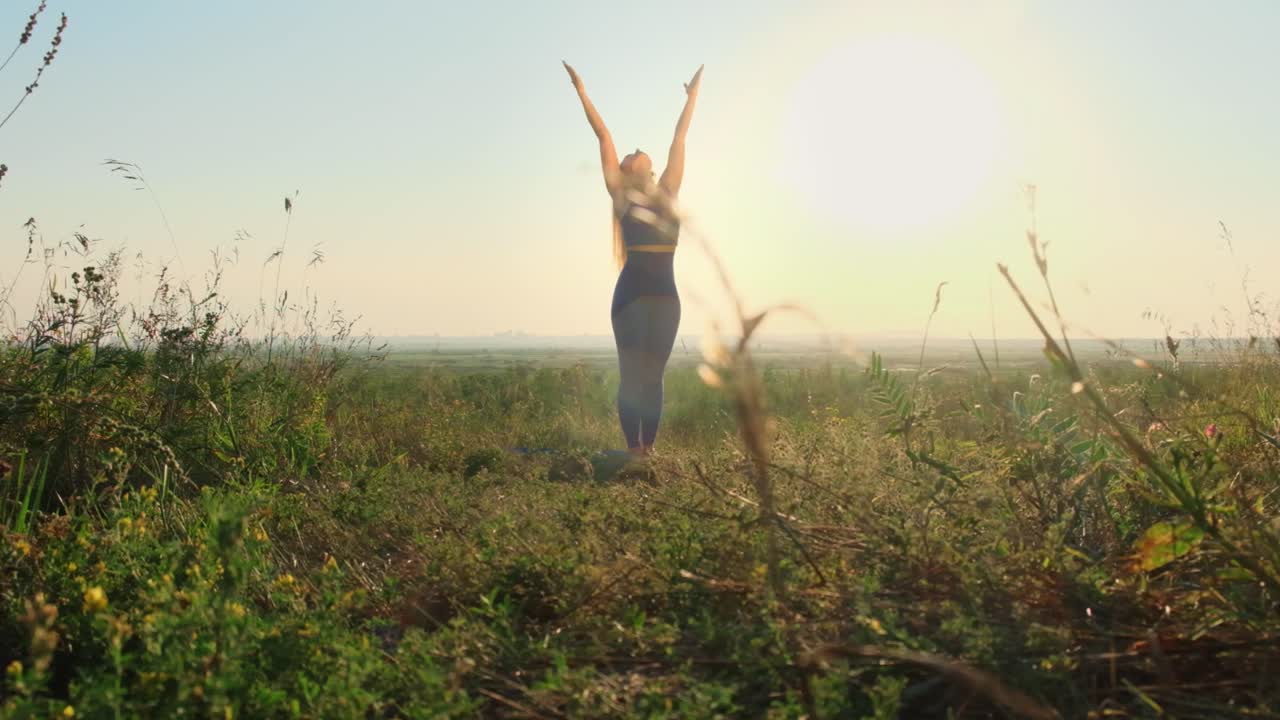 Woman practicing yoga in a field at sunrise