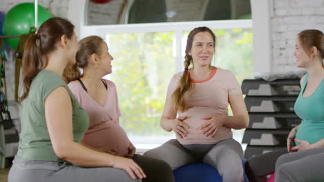 three fit pregnant women sitting in circle on yoga mats and talking