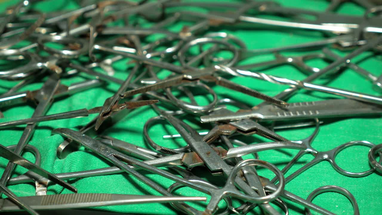 Metallic surgical tools piled on a green medical sheet in a rural Cameroonian hospital facility. Static shot