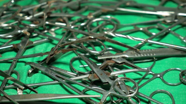 Metallic surgical tools piled on a green medical sheet in a rural Cameroonian hospital facility. Static shot