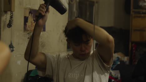 Asian-man-dries-his-hair-with-a-hair-dryer-while-looking-in-the-mirror-in-room