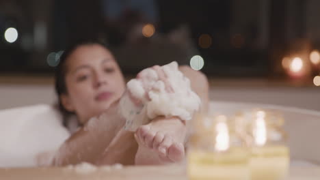 front view of a woman taking a bath while rubbing her legs with soap