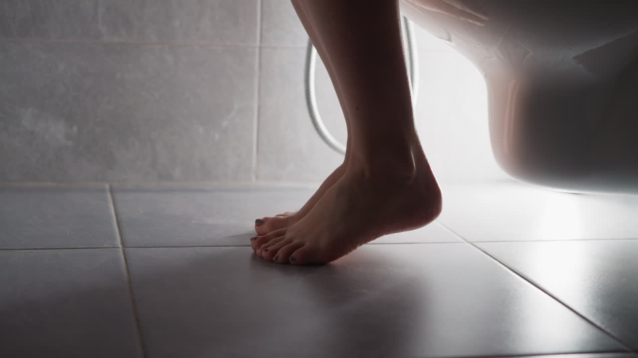 mujer se acerca al baño y se sienta en el asiento con los pies descalzos