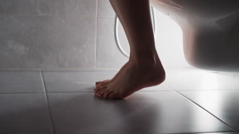 woman approaches toilet and sits on seat with bare feet