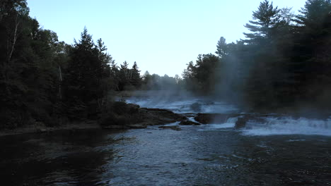 aerial drone shot over a dark misty stream and the waterfalls of big wilson falls at sunset with forest trees in silhouette