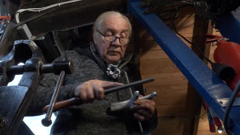 un trabajador masculino de alto rango utiliza un archivo de acero en una parte de la máquina, disparado mirando hacia arriba, taller con un vice de banco