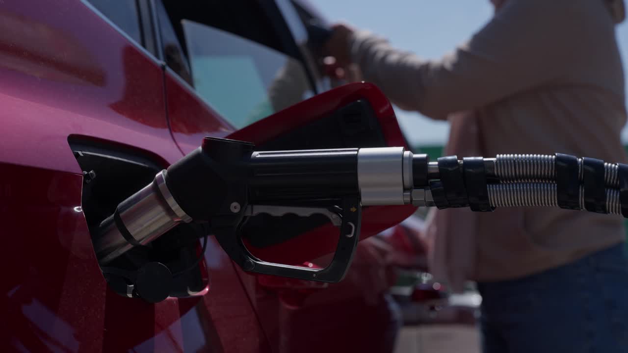 Ugello della pompa di benzina che riempie auto rossa alla stazione di servizio