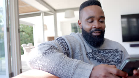 Happy-african-american-man-using-smartphone-in-sunny-living-room,-slow-motion