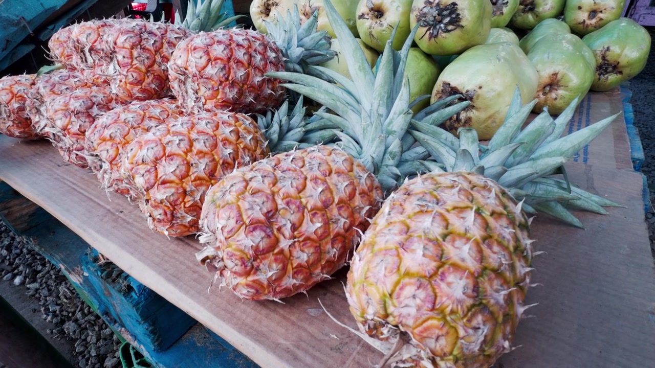 Row of fresh, ripe pineapples on display at roadside fruit stand in tropical country