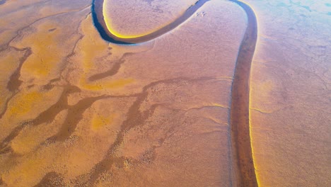 Aerial,-calm-narrow-river-channel-surrounded-by-dry-red-sand