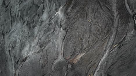 Aerial-top-down-riverbed-glacial-river-flowing-through-black-natural-volcanic-landscape