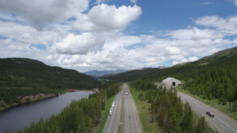 hd aerial drone shot of interstate 70 i-70 near vail colorado usa during summer day with traffic driving on road next in forest landscape and cloudy blue sky