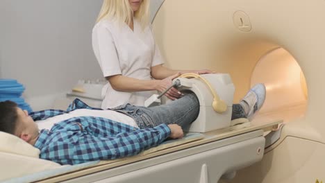 woman doctor makes knee-joint mri scanning. young man patient on automatic table enters into a closed-type mri machine using noise isolation headphones. modern equipment, coil on the patient's knee