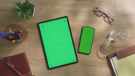 office workspace with tablet and smartphone green screens