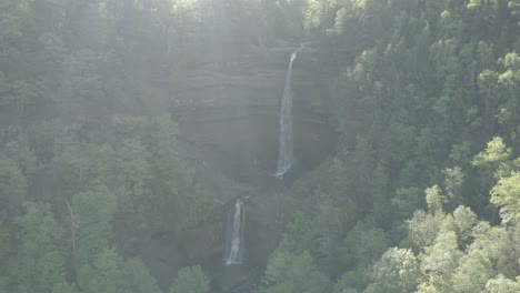 Drone-shot,-showing-2-waterfalls,-while-having-sunlight-coming-over-the-top-of-the-trees