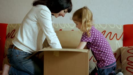 family, mom and daughter opens the parcel from the online store. young woman looks in the box, is surprised and happy to receive a surprise. girl opened a box with a gift. slow motion.