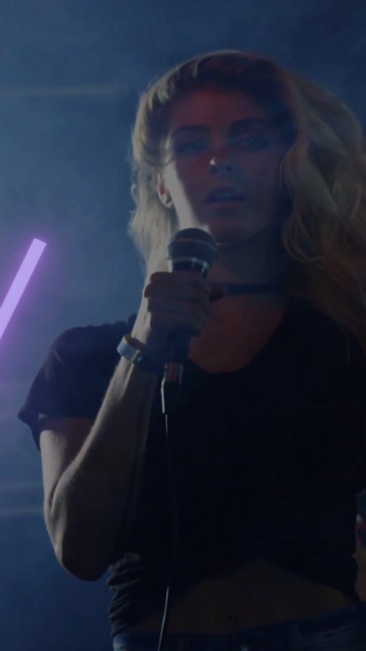 Video verticale: Cantante che inclina la testa mentre un tubo al neon viola scorre, tenendo un microfono con filo per la musica