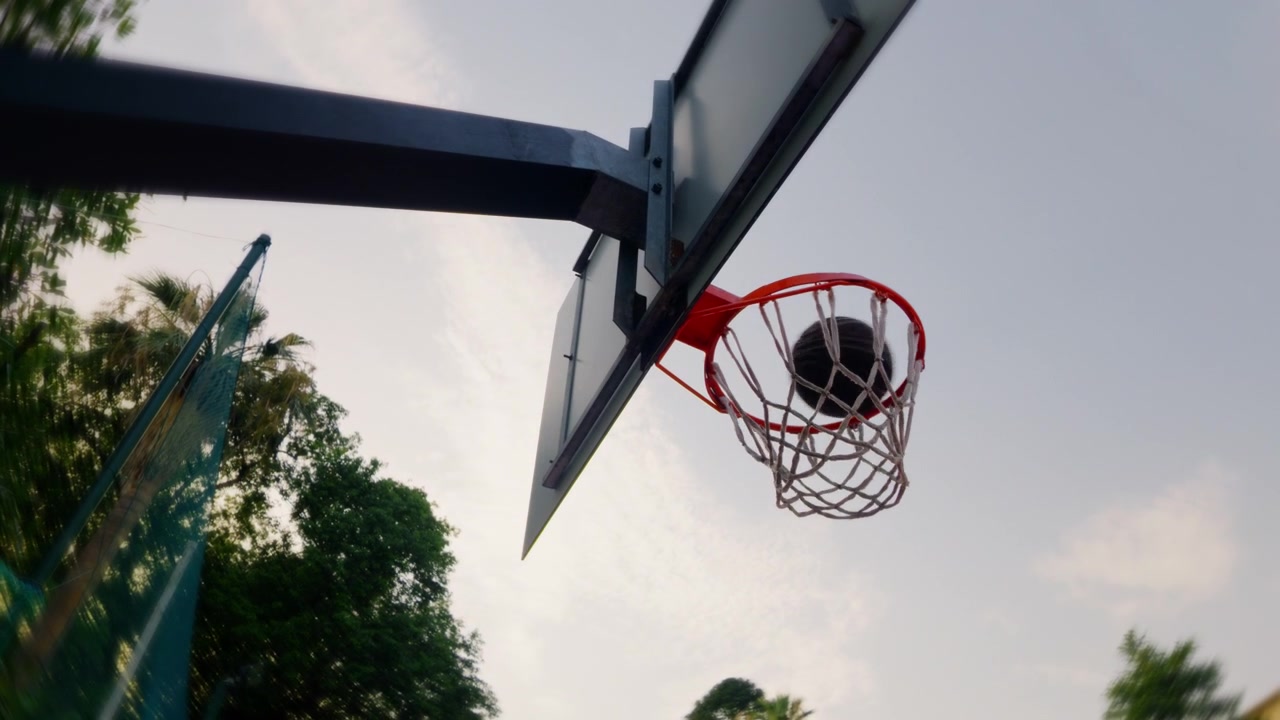 Un pallone da basket cade attraverso un canestro esterno al rallentatore, visto dal basso al tramonto