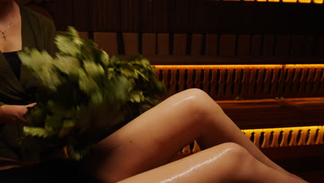 woman receiving a banya treatment with herbal broom in a wooden sauna