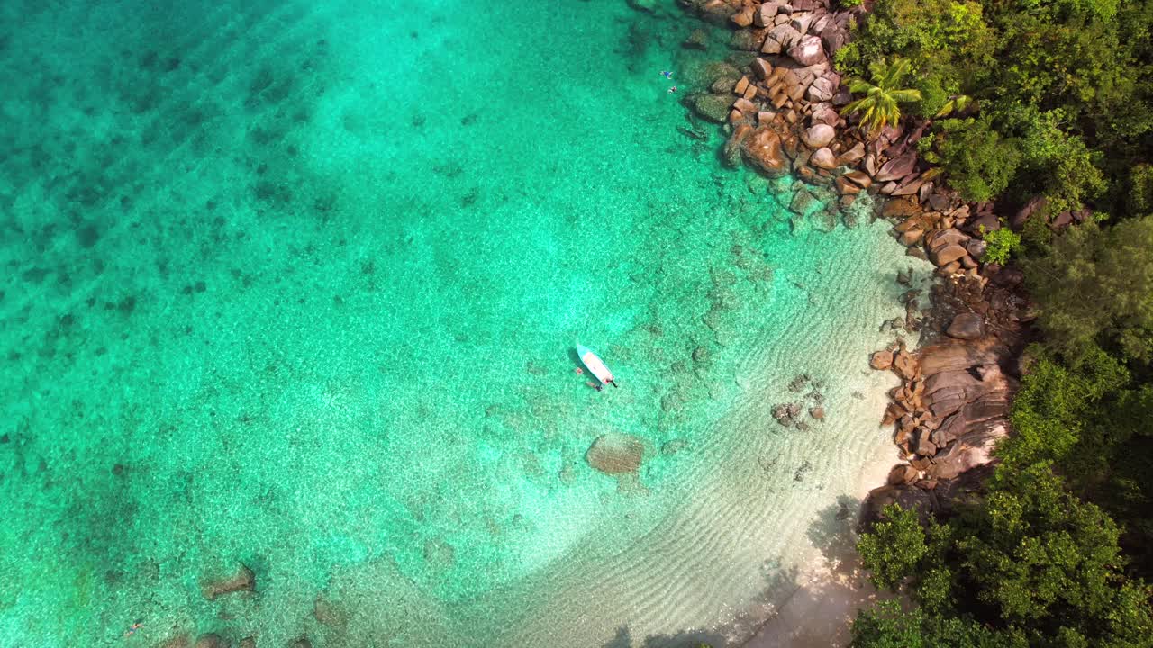 Drone Pantai Anse Major, pandangan mata burung terbang di atas 4 turis yang snorkeling dekat perahu, batu granit, air pirus, dan pantai berpasir putih, Mahe Seychelles 30 fps.