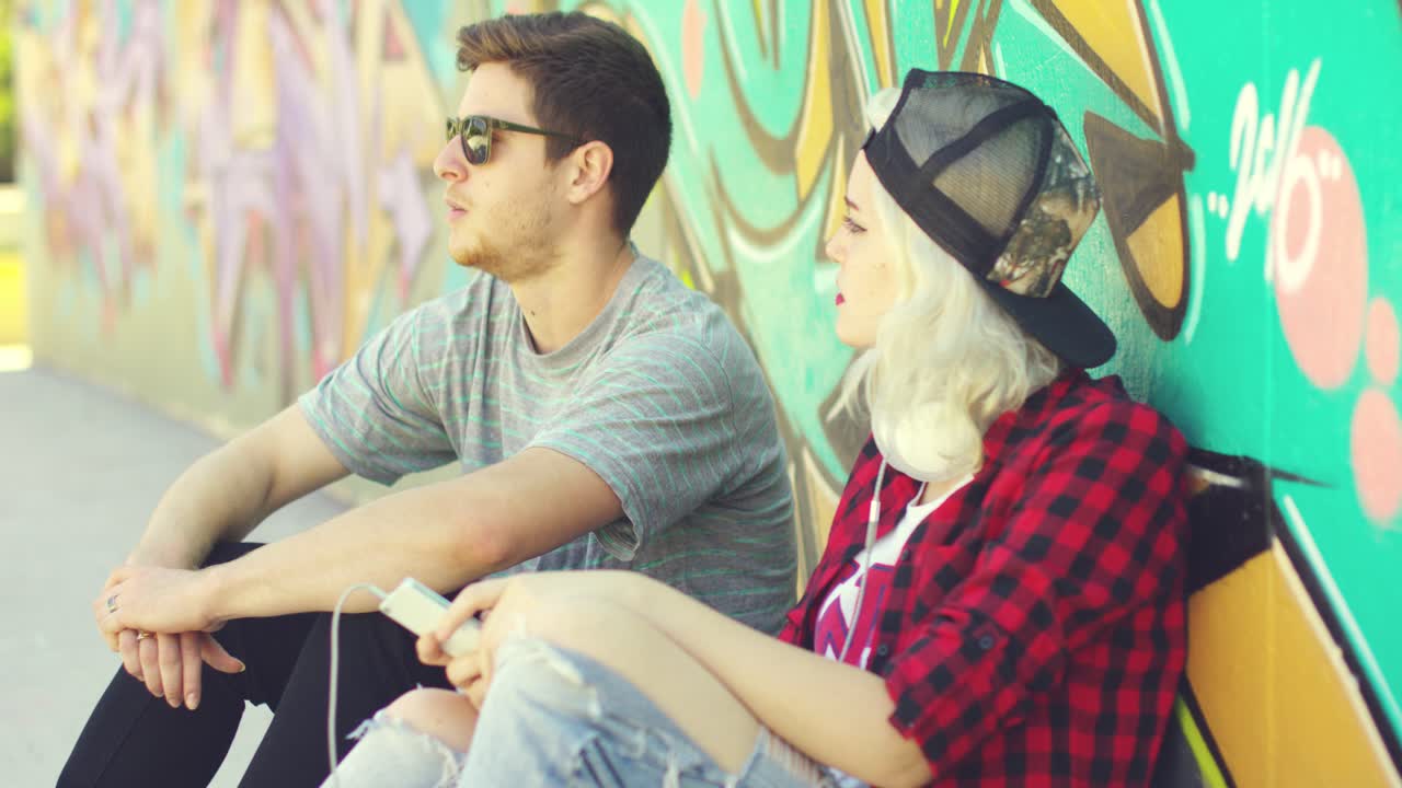pareja hipster relajándose contra una pared de graffiti
