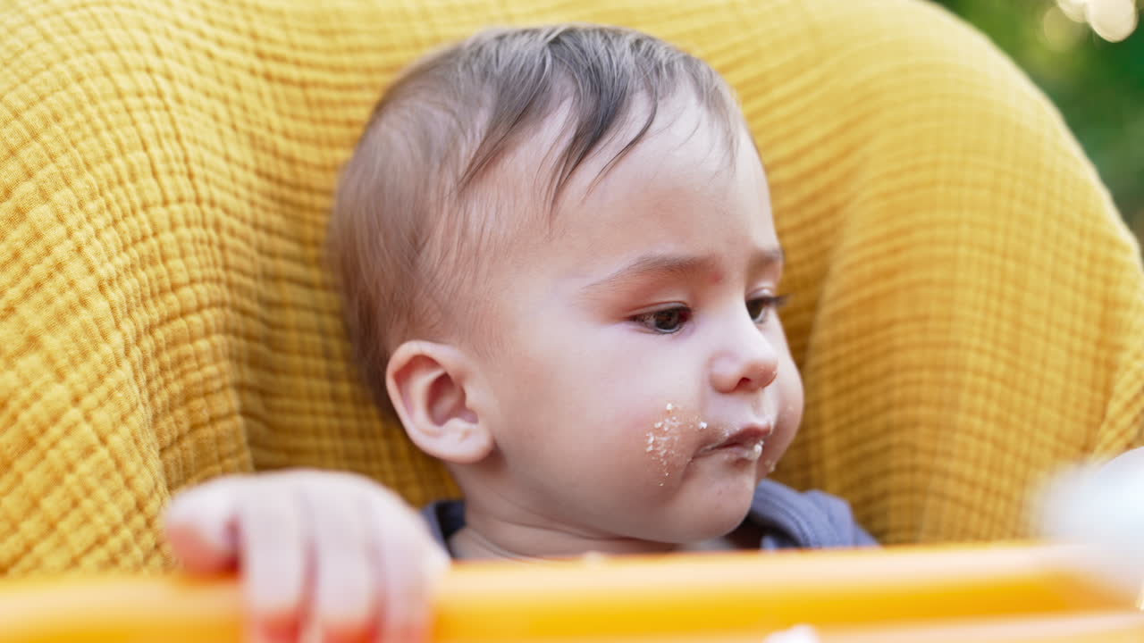 Baby nutrition from spoon. Cute Caucasian child with smudged face eating porridge. Close up. Blurred backdrop.