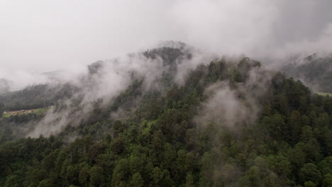 Aerial-shot-of-a-mountain-with-trees-covered-by-low-clouds-with-a-small-town-in-the-background-in-Valle-De-Bravo,-Mexico