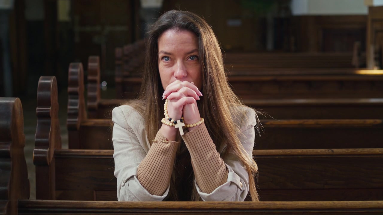 Mulher Devota Sentada em Oração num Banco de Igreja com Olhos Fechados e Mãos Postas Segurando um Terço