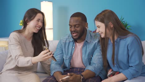 young people of different races looking at the phone at home and laughing.