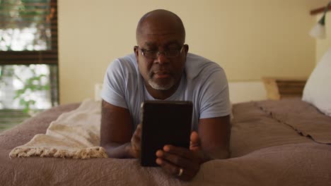 Glücklicher-Afroamerikanischer-älterer-Mann,-Der-Auf-Dem-Bett-Liegt-Und-Sich-Mit-Einem-Tablet-Entspannt