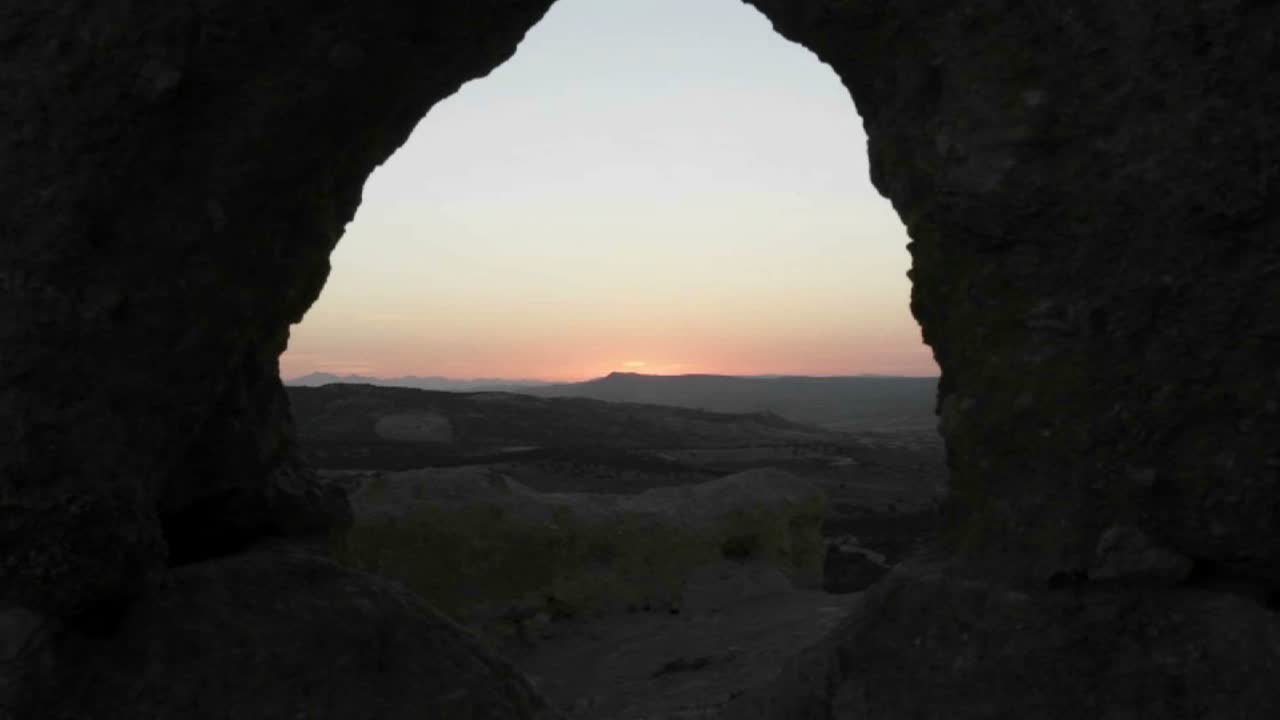 se ve el sol saliendo a través de una cueva y sobre montañas superpuestas